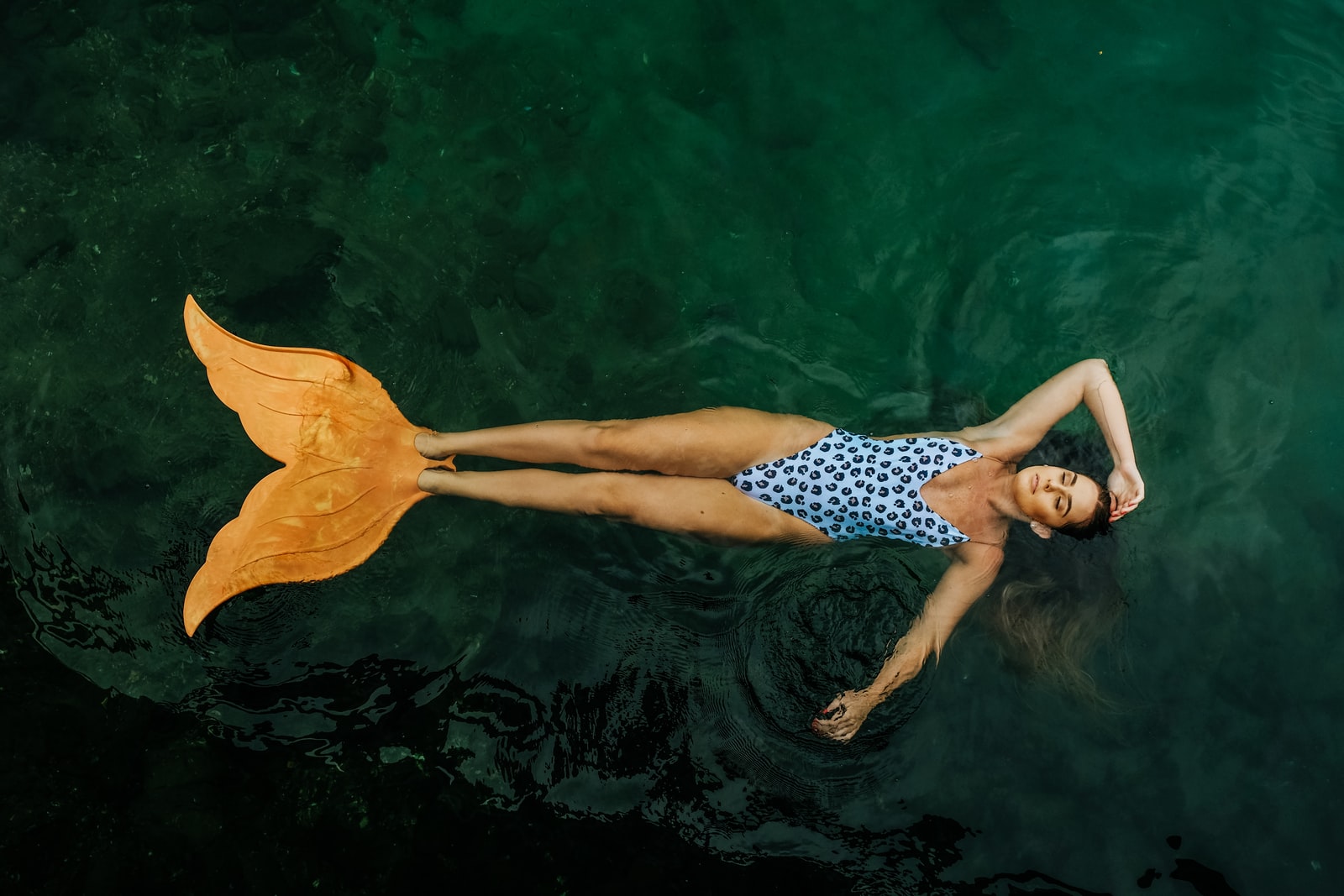 photo of woman floating on body of water with mermaid tail flippers